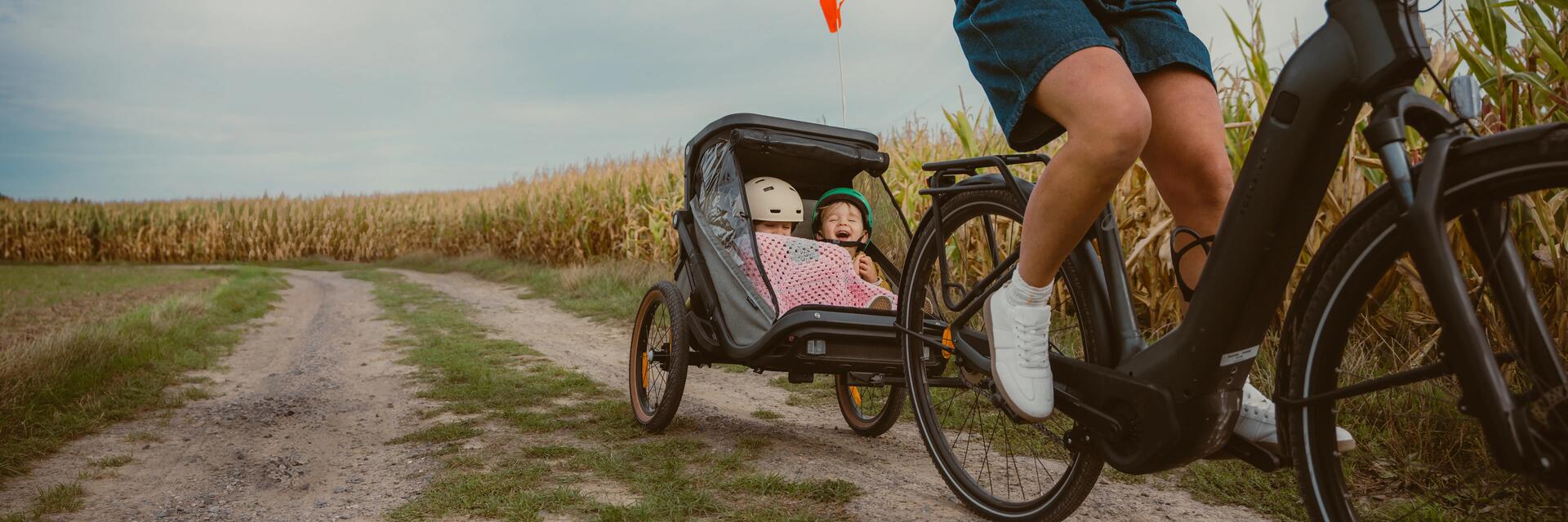 Kobieta jadąca rowerem z przyczepką z dziećmi w terenie