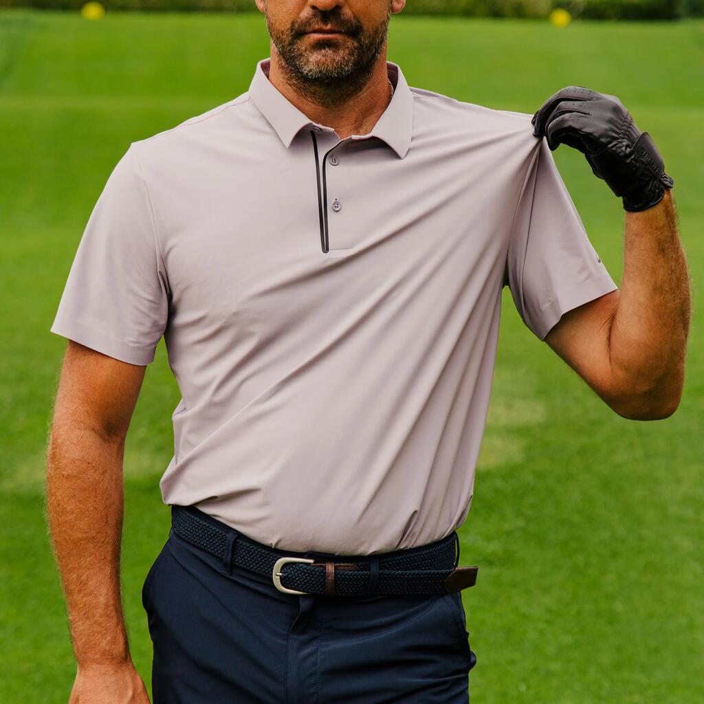 Ein Mann im weinroten Poloshirt und mit Golfhandschuh blickt auf einem Rasenplatz vor Palmen aufmerksam in die Ferne.
