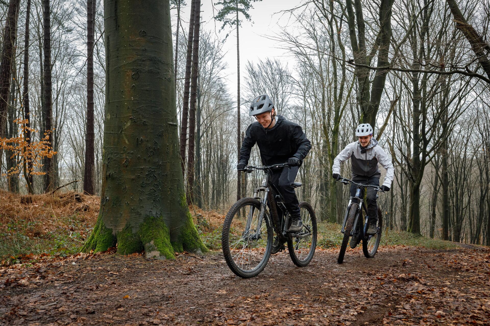 2 homens a pedalar em btt no meio de árvores
