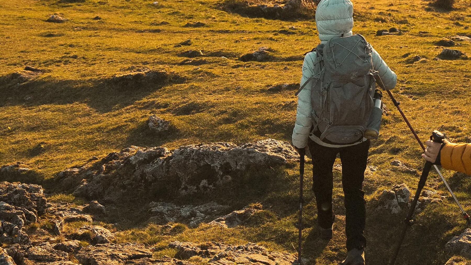 Kobieta z kapturem na głowie z plecakiem i kijkami uprawiająca trekking
