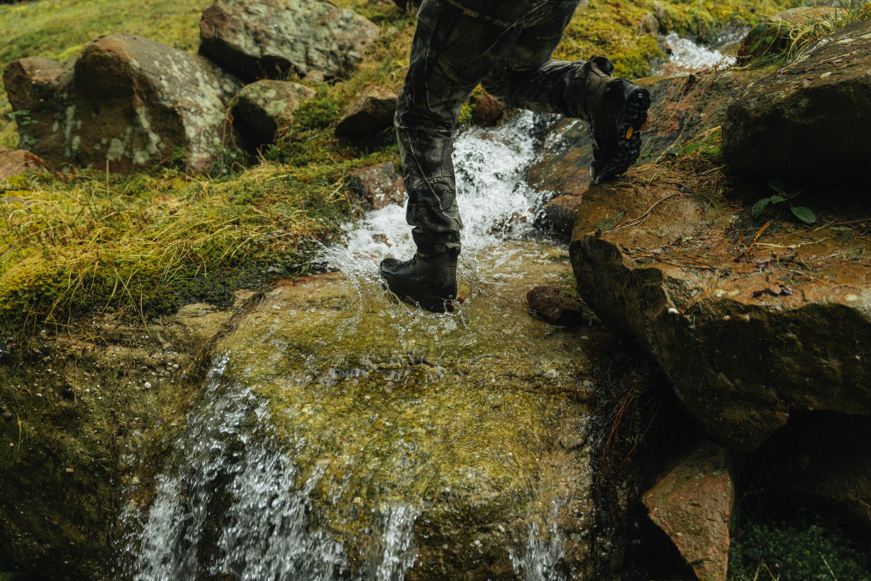 Un chasseur franchit un petit ruisseau en mettant le pied dans l'eau