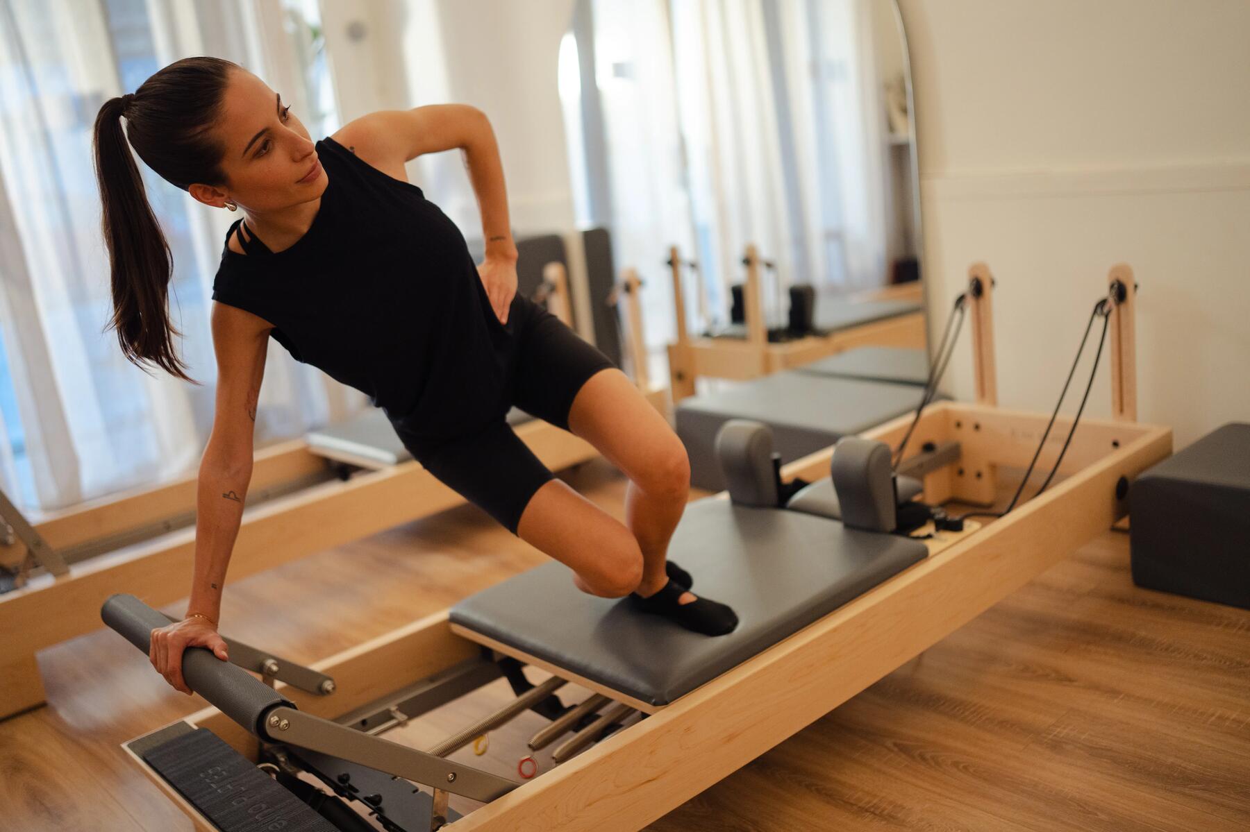 Frau in schwarzer Fitnessbekleidung beim Reformer Pilates in hellem Raum