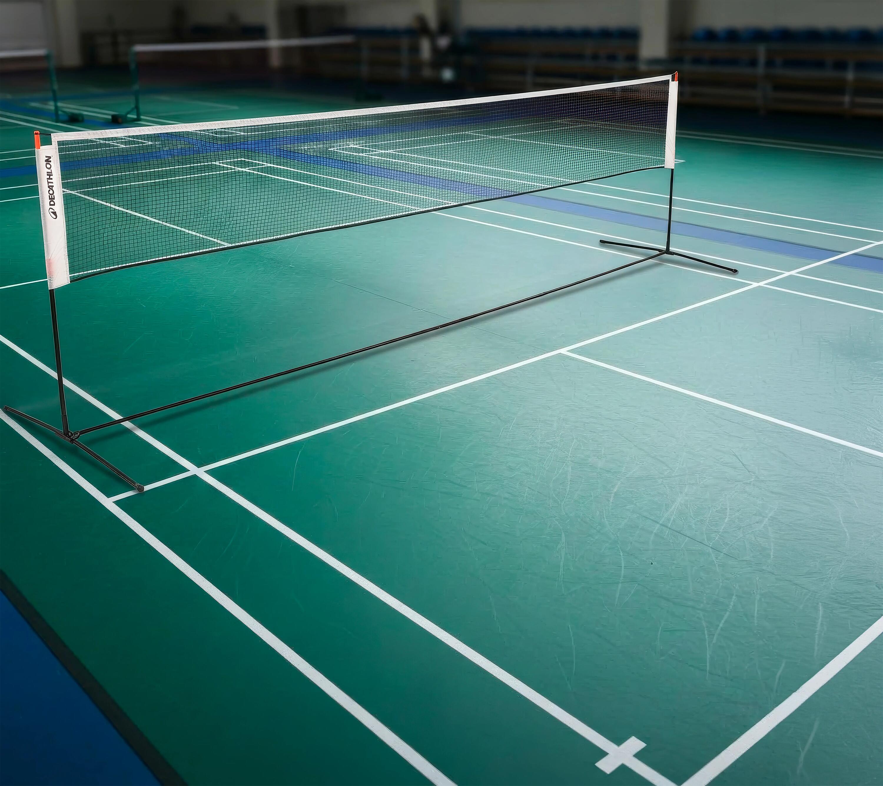 Tragbares Decathlonnetz auf schwarzem Gestell, aufgebaut auf dem grünen Boden einer Sporthalle mit weißen Spielfeldlinien.