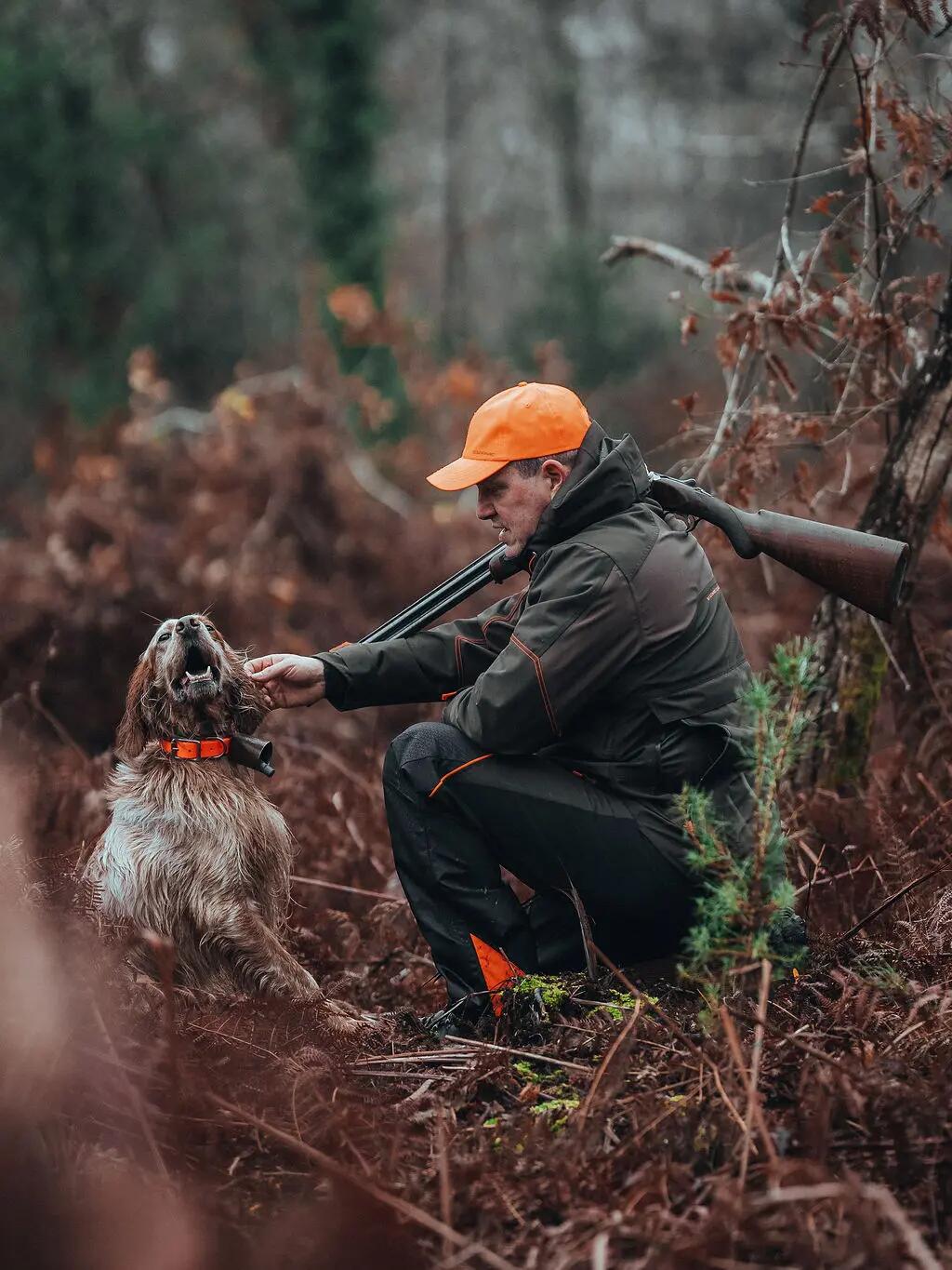 EIn Jäger kniet im Wald bei Regenwetter und streichelt seinen Hund