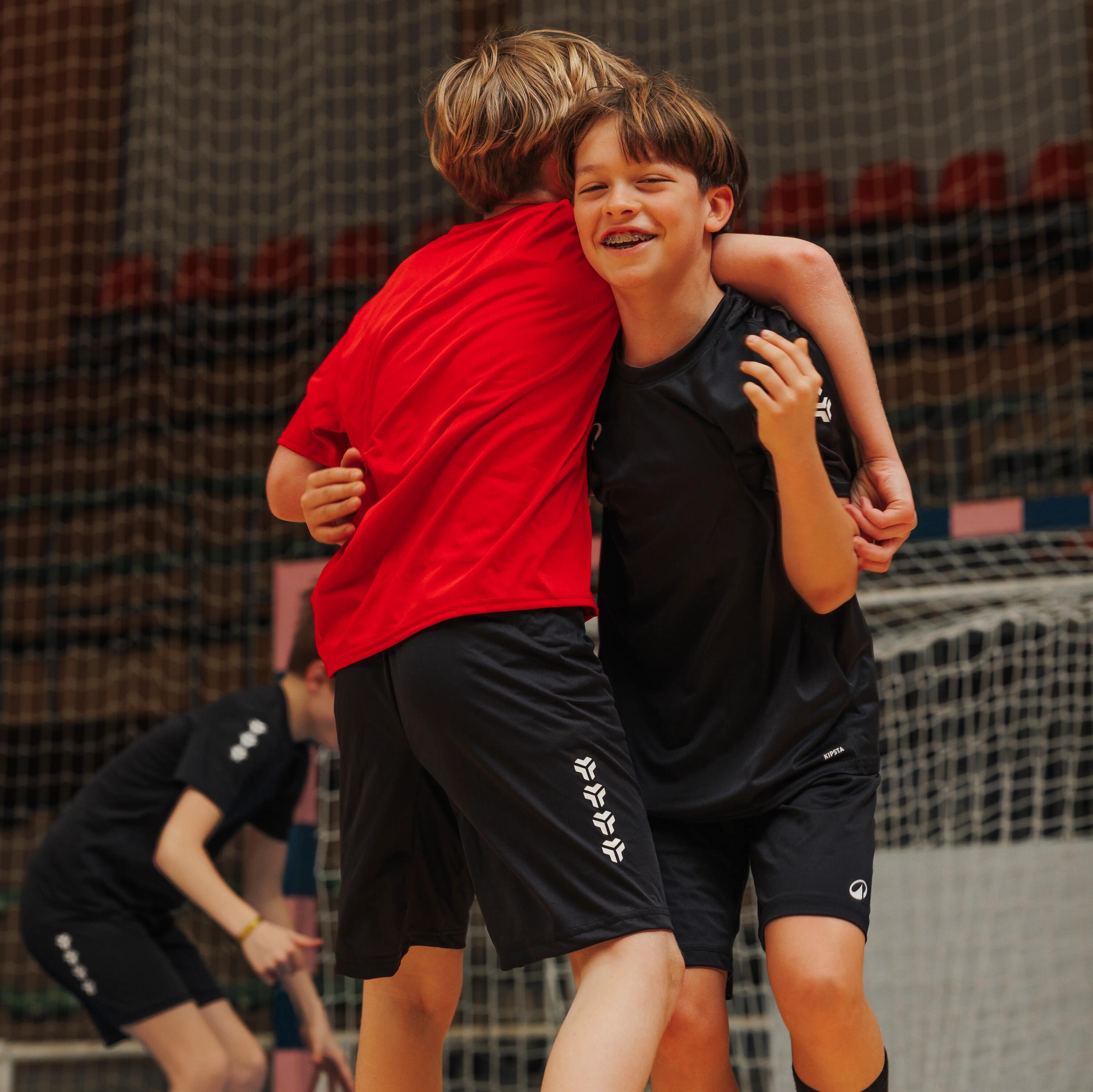 Kinder tragen umklammern sich in der Halle und tragen Kipsta Handball Bekleidung.