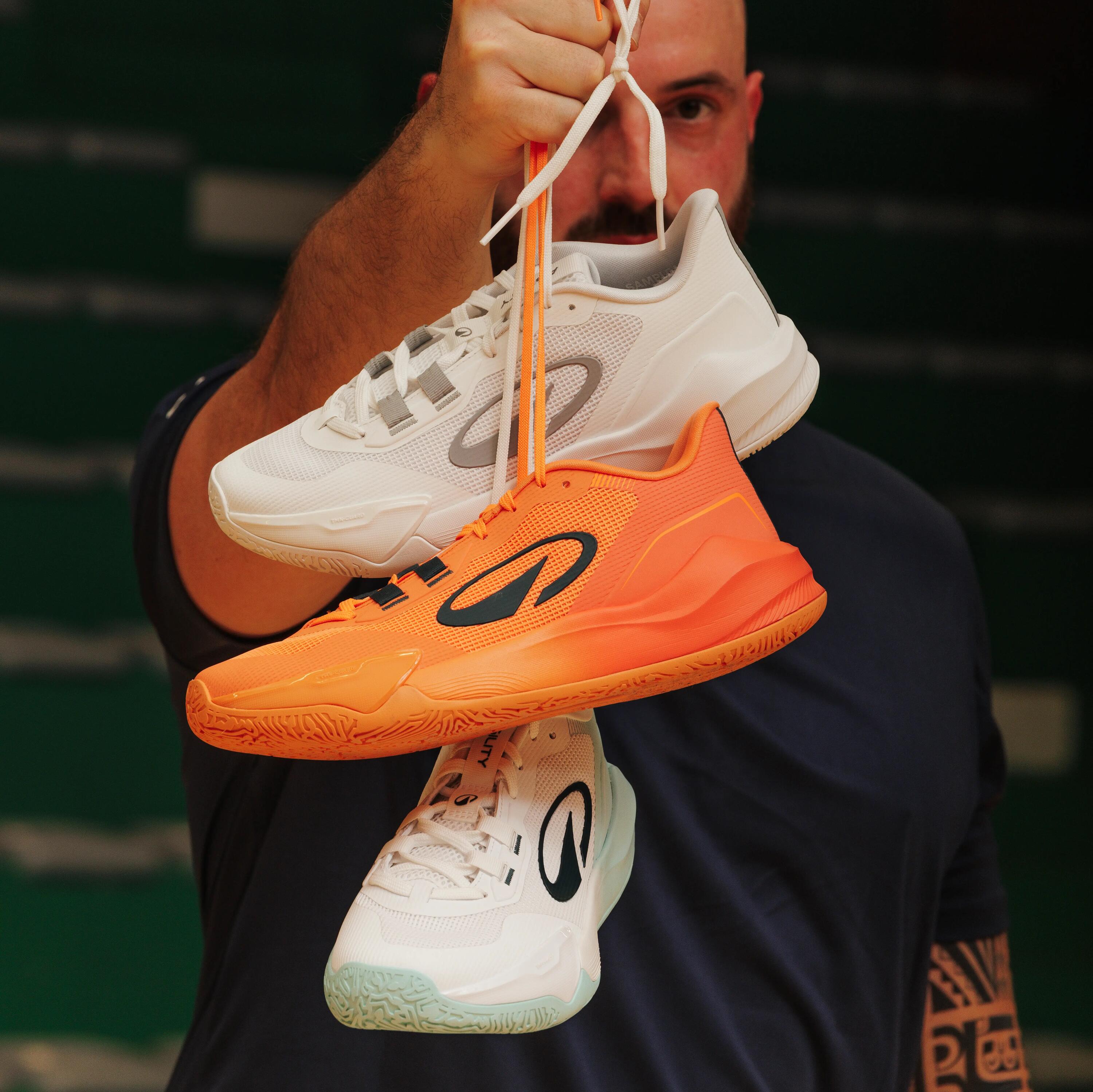 Mann hält verschiedenfarbige Kipsta Handballschuhe H500 am Schnürsenkel in die Kamera.