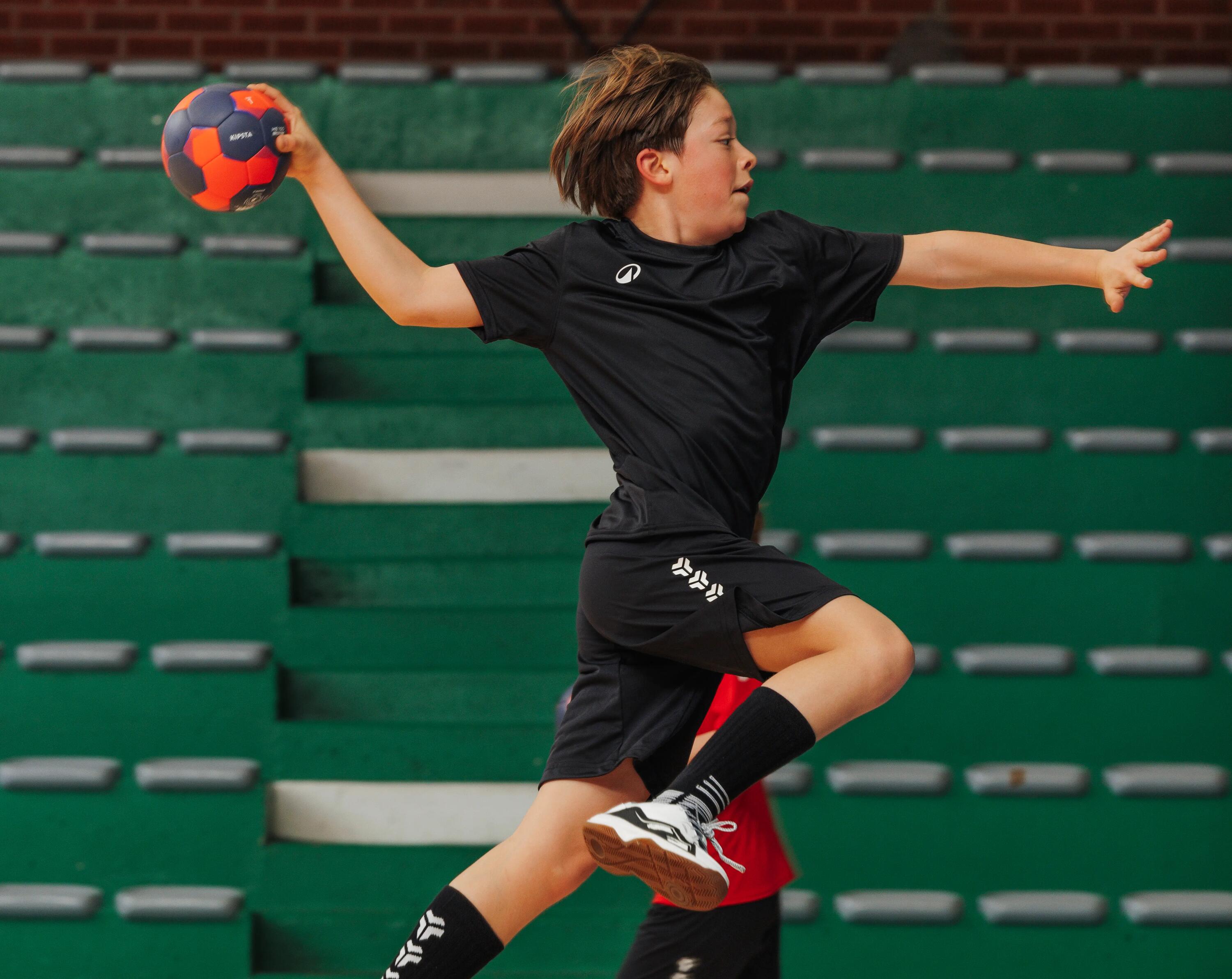 Junge wirft im Sprung einen Handball in Decathlon Ausstattung.