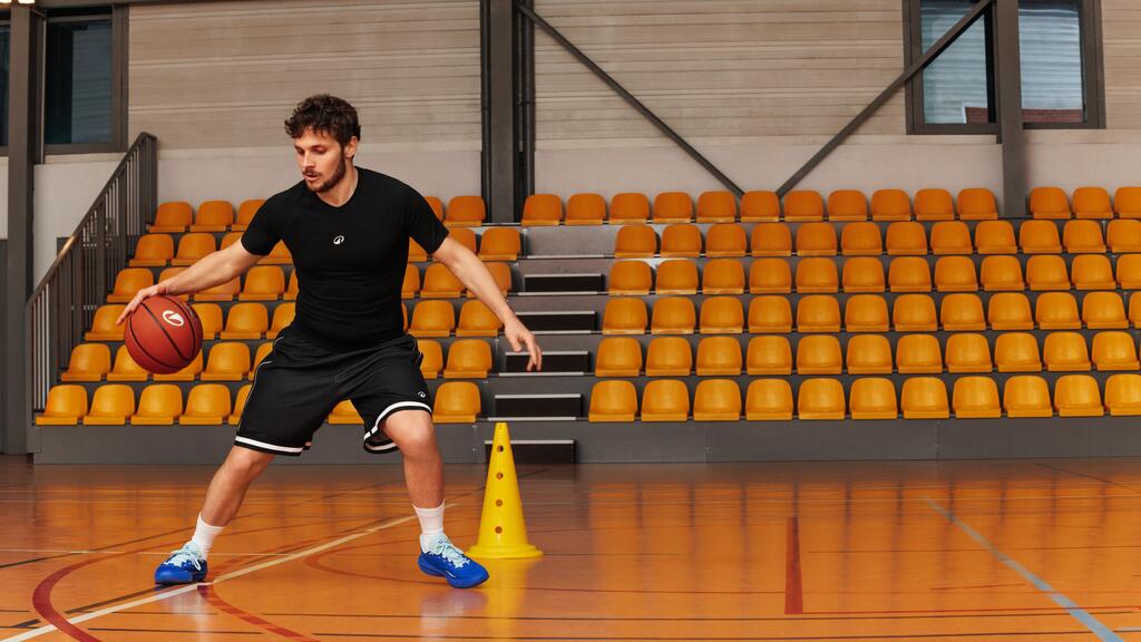 Ein Mann spielt Basketball in einer Halle mit gelben Sitzplätzen im Hintergrund