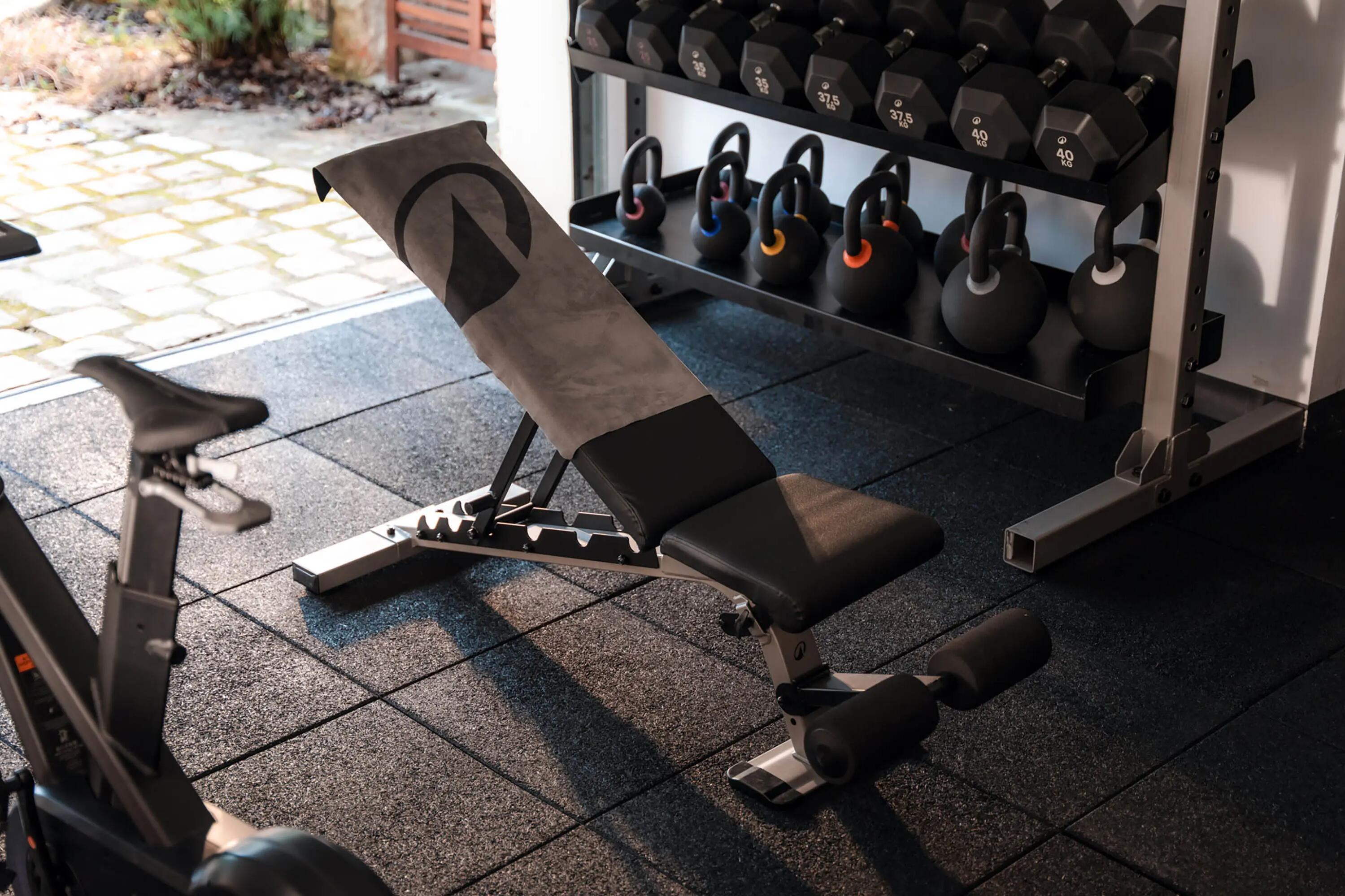Schrägbank mit Handtuch in einem Fitnessraum vor einem Regal mit Kettlebells und Kurzhanteln.