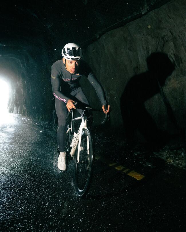 Mann mit Radtrikot und Radhose im Dunkeln bei Regen auf einem Rennrad