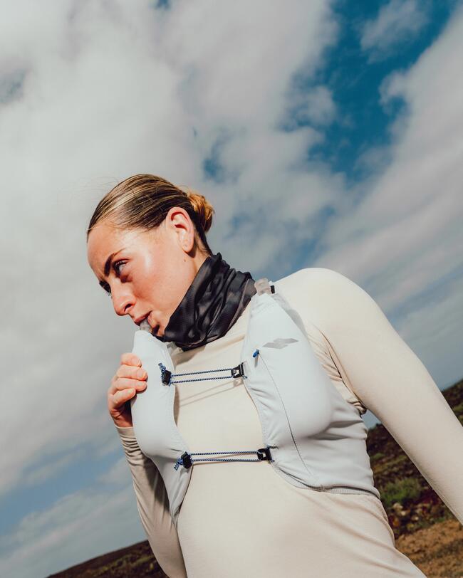 Eine Athletin in Sportkleidung trinkt aus einer Laufweste unter freiem Himmel.