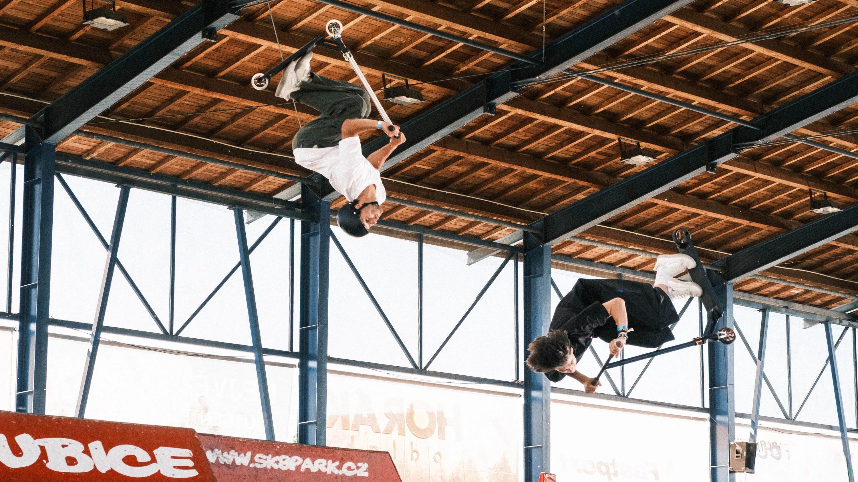 Zwei Stuntscooter-Fahrer zeigen in einer Skatehalle spektakuläre Sprünge und Tricks hoch über den Rampen. Das Bild fängt pure Dynamik, Action und die extremen Belastungen ein, denen ein Stuntscooter standhalten muss.