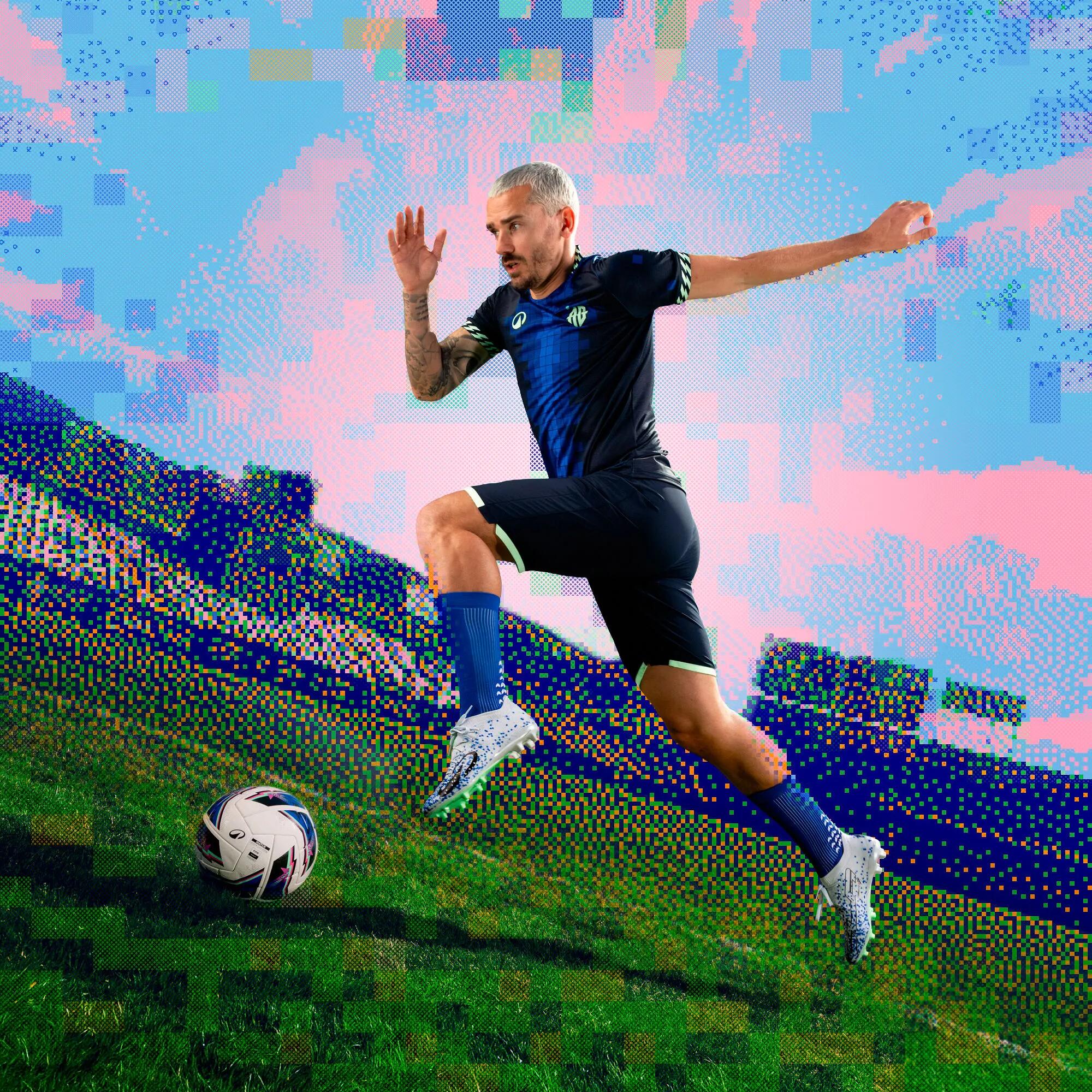 Jogador de futebol em equipamento azul e branco a rematar a bola num relvado verde.