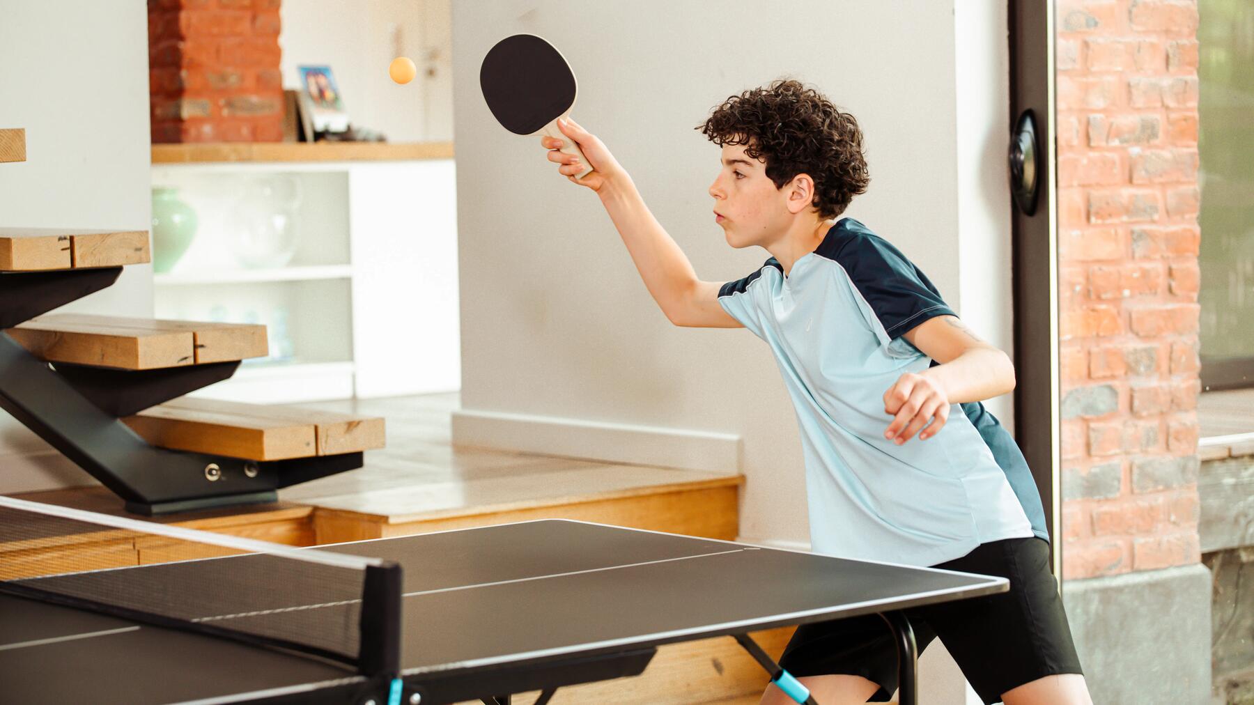 Ein Junge spielt mit Tischtennis mit Schläger in der Wohnung