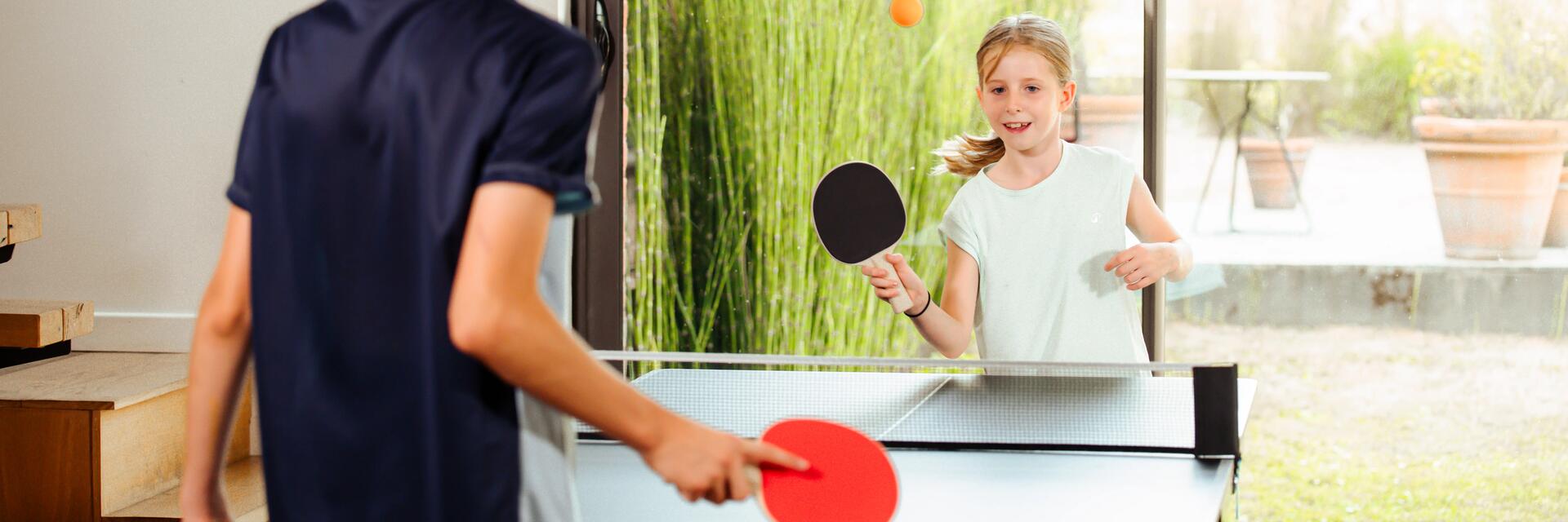 Zwei Geschwister spielen mit den richtigen Schlägern Tischtennis im Wohnzimmer