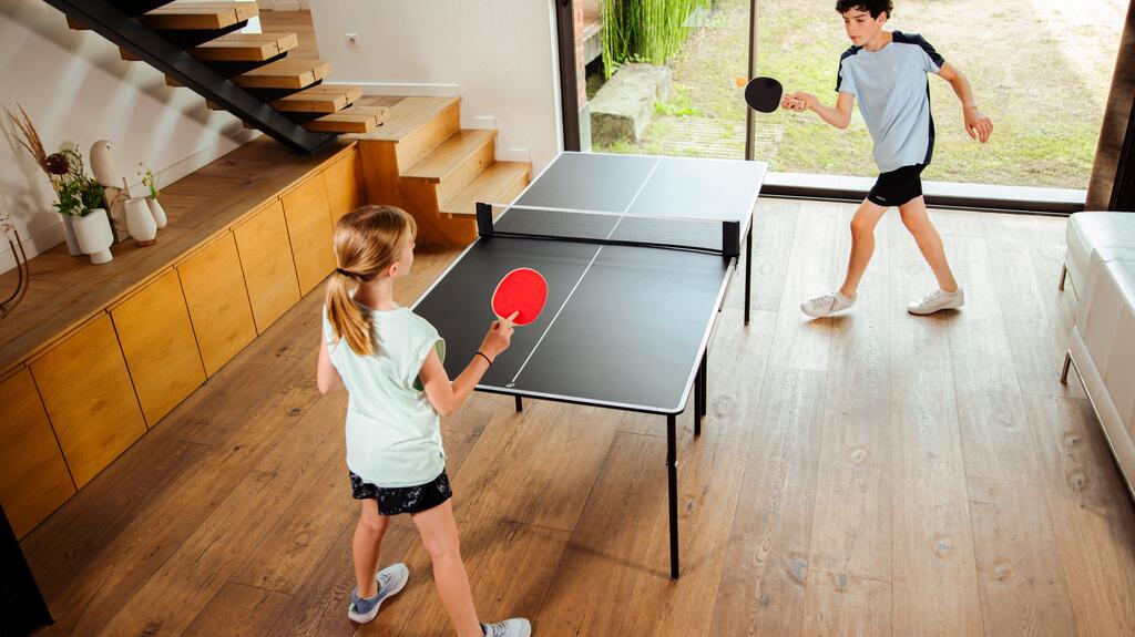Zwei Kinder spielen in einem Wohnzimmer Tischtennis an einer kompakten Indoor-Tischtennisplatte.