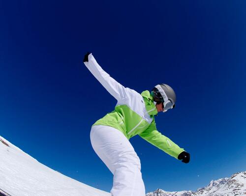 kobieta w odzieży i butach snowboardowych robiąca trik na desce snowboardowej