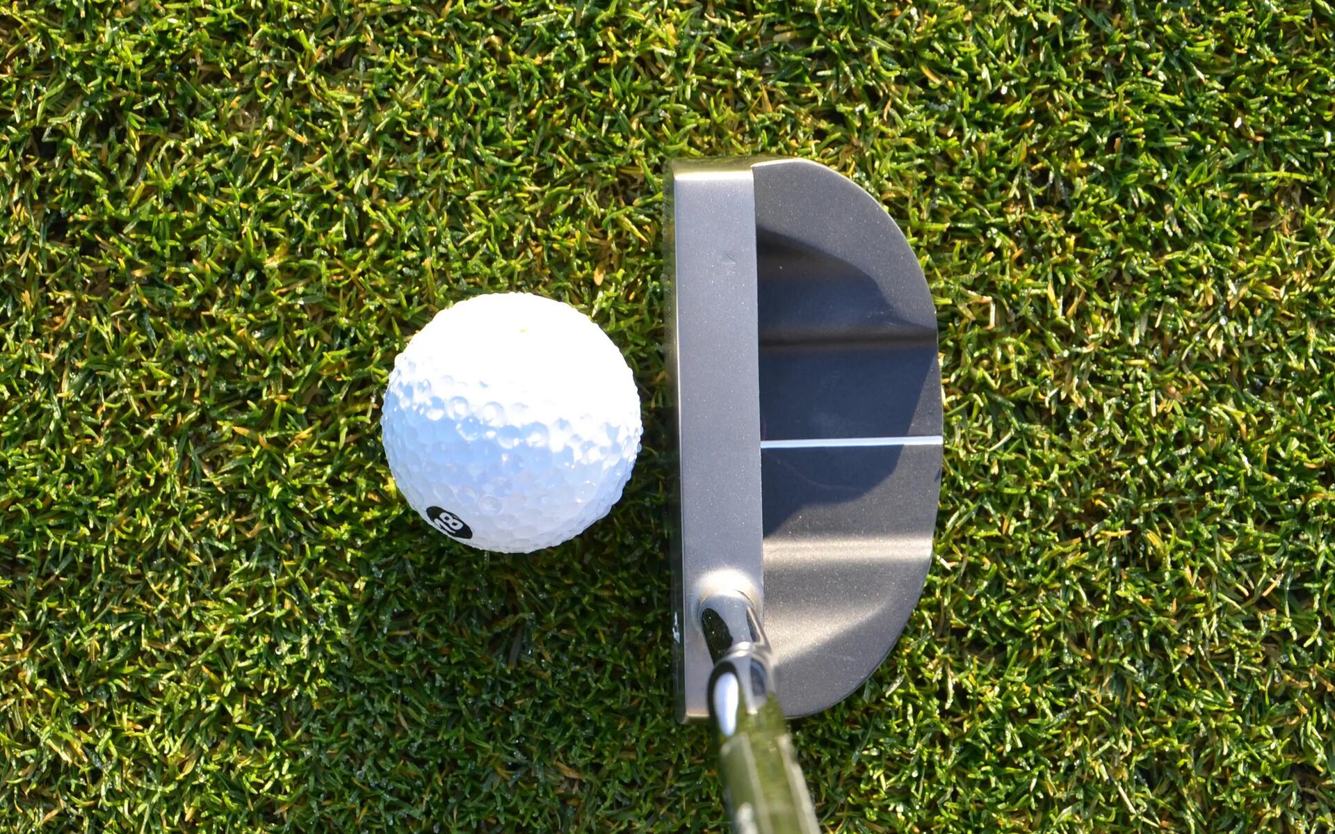 piłeczka golfowa leżąca na trawie obok kija golfowego