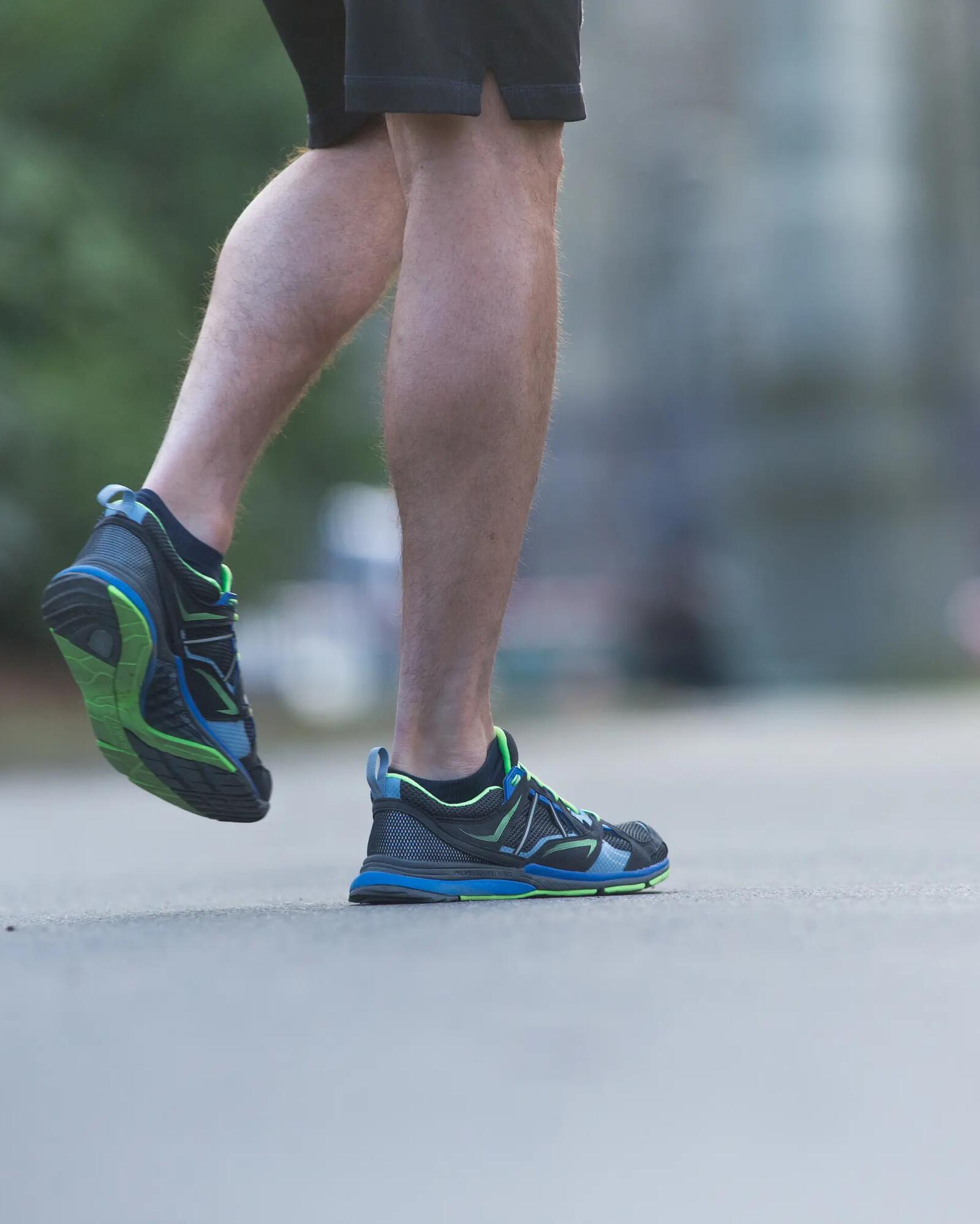 Nahaufnahme der Beine und Füße eines Läufers in blau-schwarzen Sportschuhen auf asphaltiertem Weg.