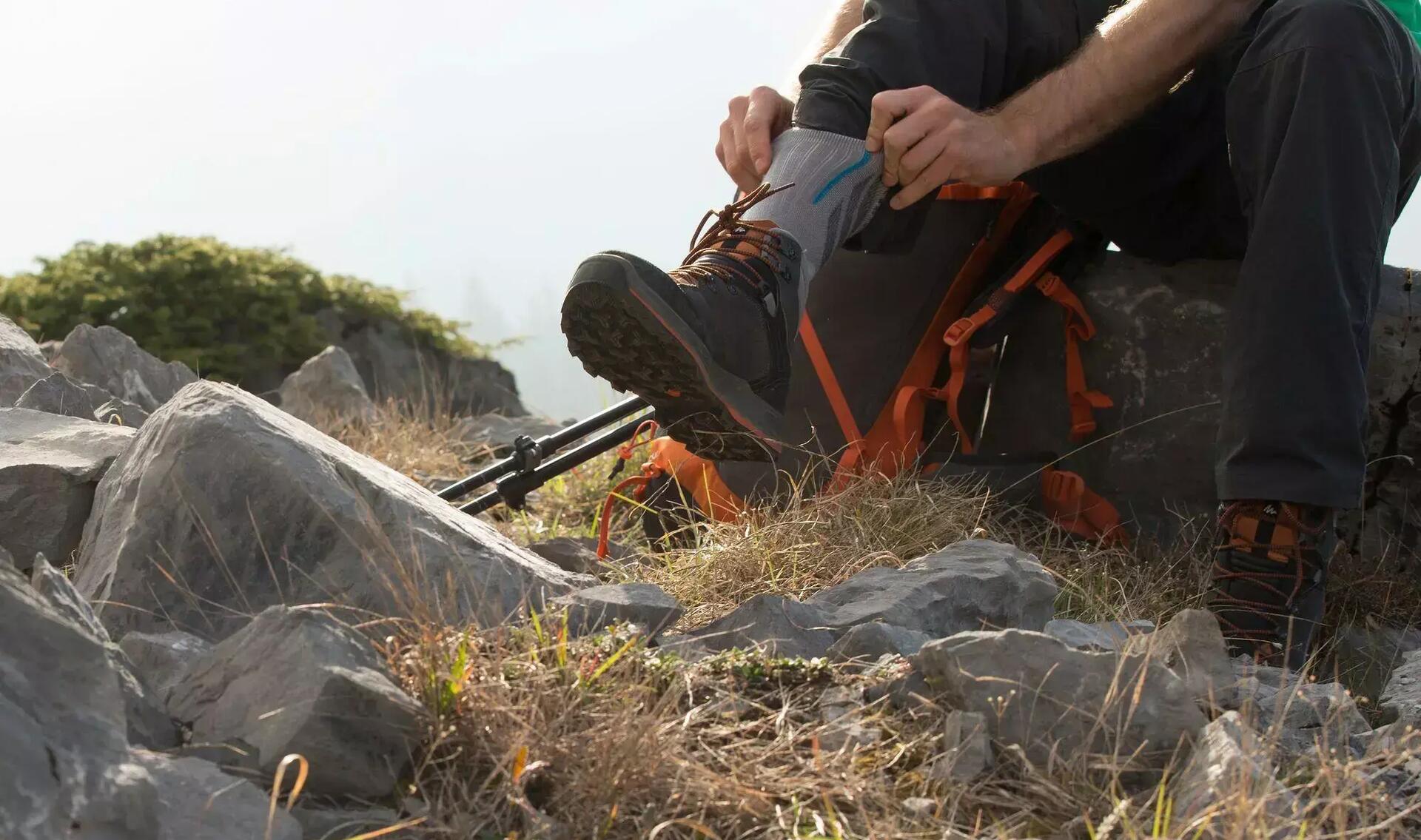 mężczyzna podciągający skarpety w góry siedząc na kamieniu w butach trekkingowych