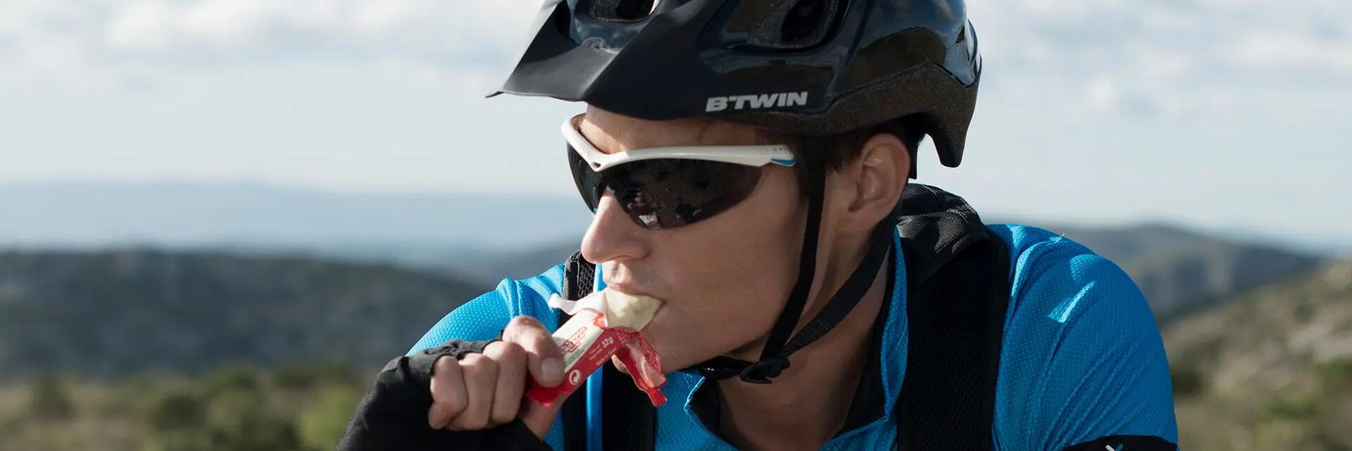 Mężczyzna w kasku i w okularach jedzący baton proteinowy na rowerze