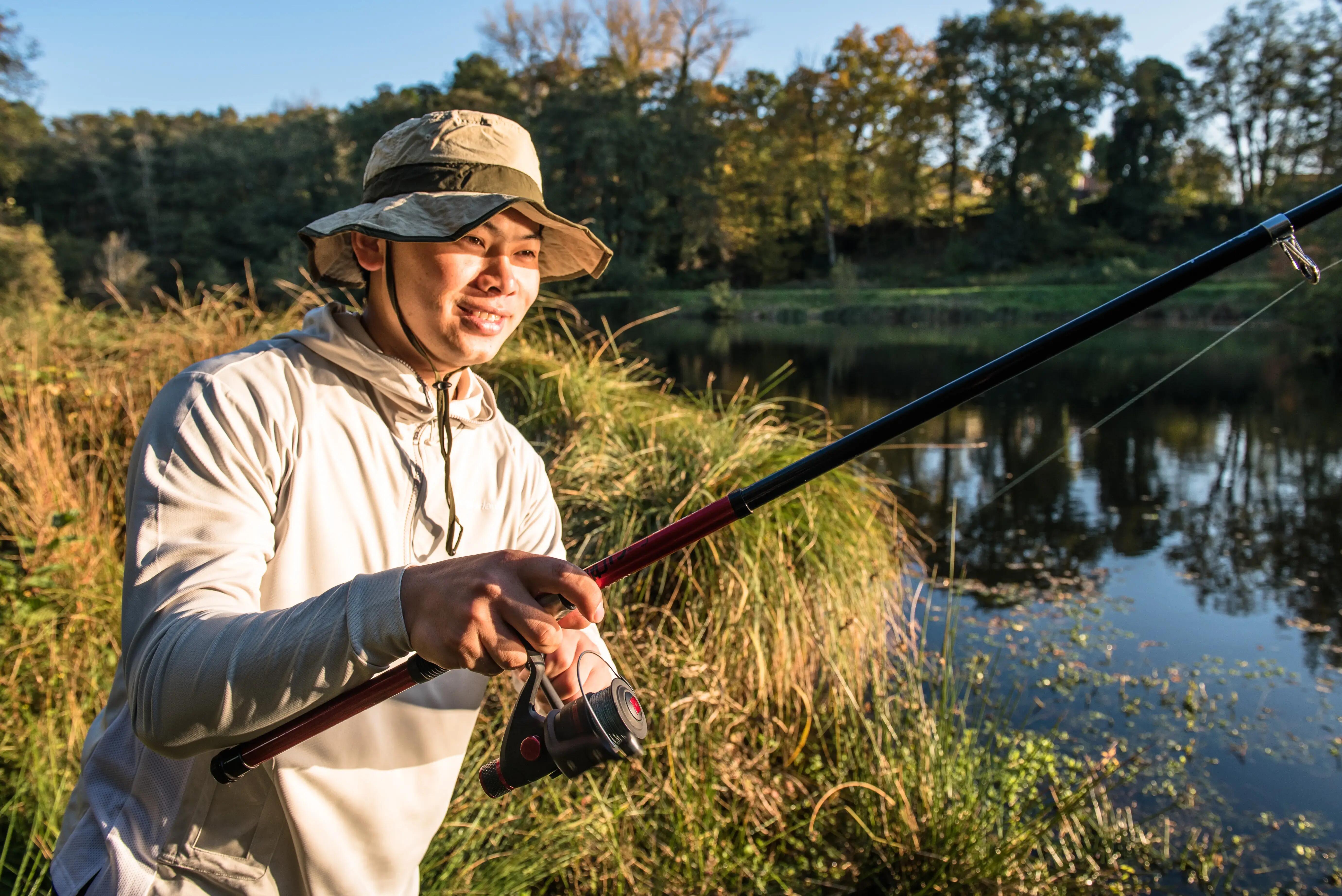 Angler wearing a fishing hat while casting beside a lake