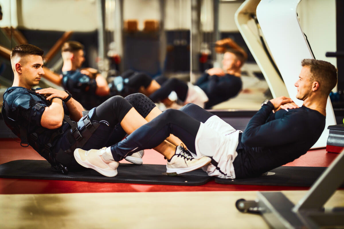 Mężczyźni w odzieży fitness wykonujący ćwiczenia na macie podczas treningu EMS