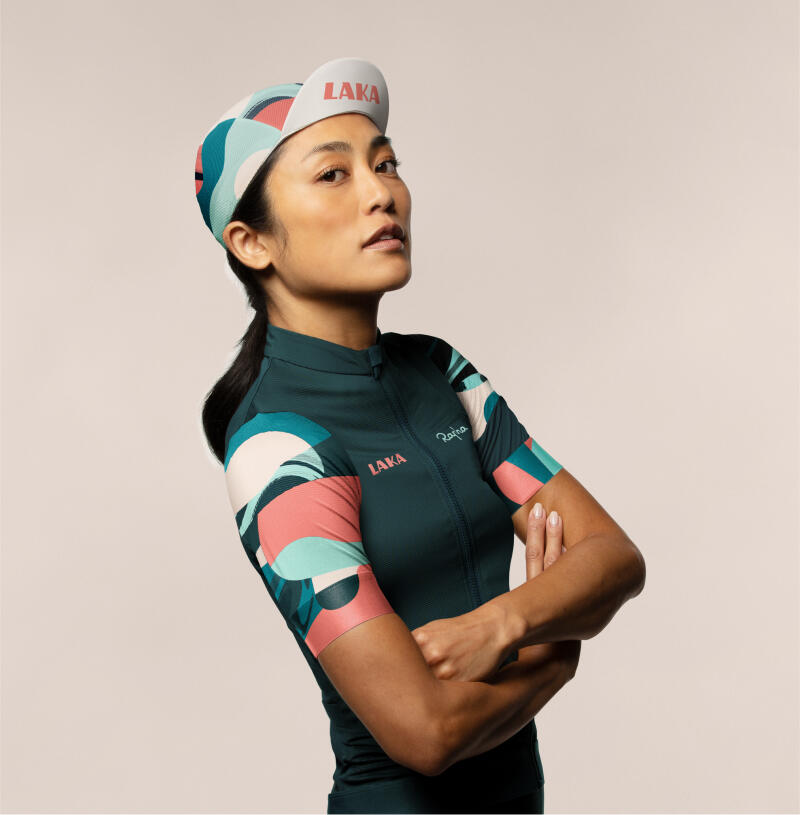 Radfahrerin in buntem Trikot mit geometrischen Mustern in Grün, Rosa und Weiß. Modernes, sportliches Outfit.