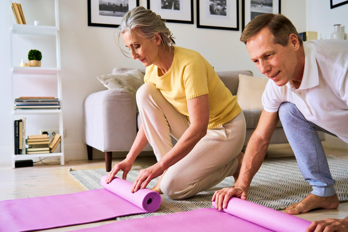 Seniorzy rozwijający matę do jogi aby wspólnie ćwiczyć w domu