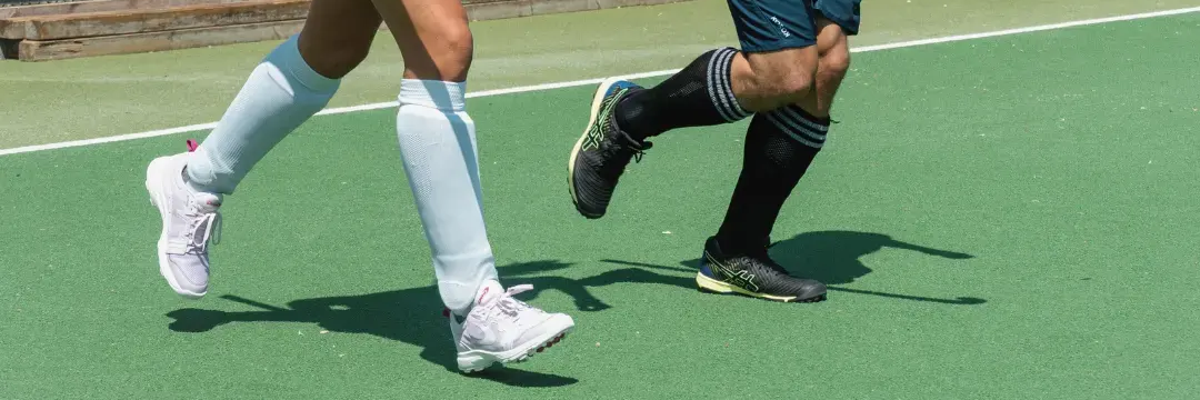 Twee hockeyspelers met scheenbeschermers aan op een hockeyveld