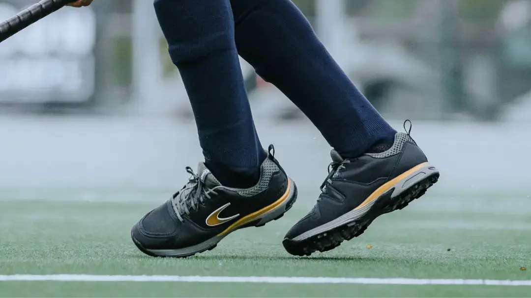 Iemand met veldhockeyschoenen aan speelt hockey op een buitenveld