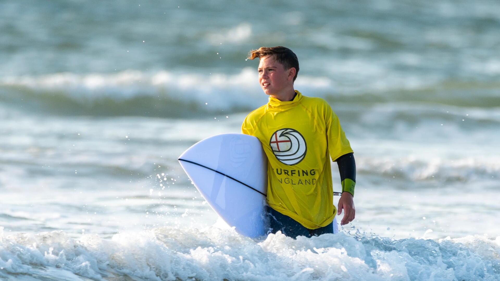 Young boy in the water, while carrying his surfboard.