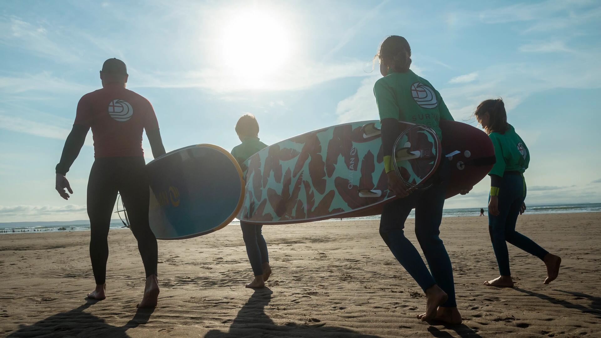 4 people carrying their surfboards to the water