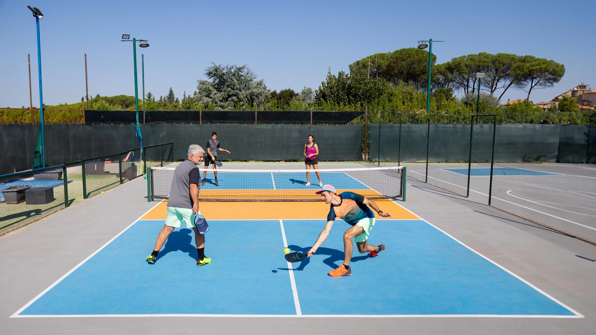 Grupa ludzi w strojach sportowych grająca w pickleballa na korcie 