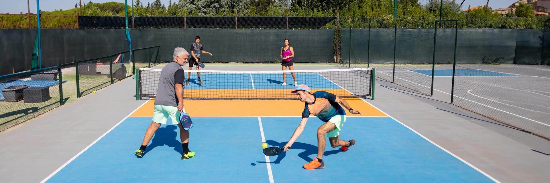 Grupa ludzi w strojach sportowych grająca w pickleballa na korcie