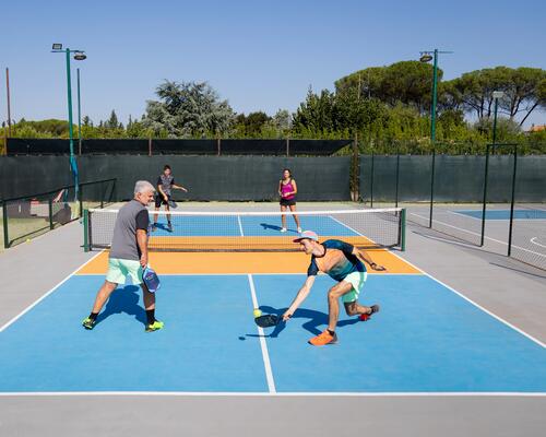 Grupa ludzi w strojach sportowych grająca w pickleballa na korcie