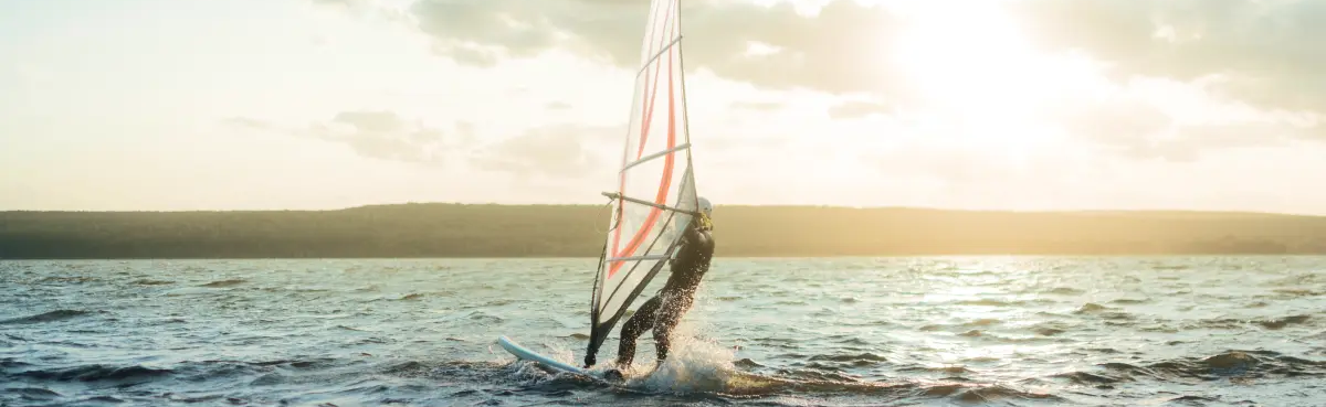 osoba płynąca na desce windsurfingowej trzymając  żagiel  windsurfingowy