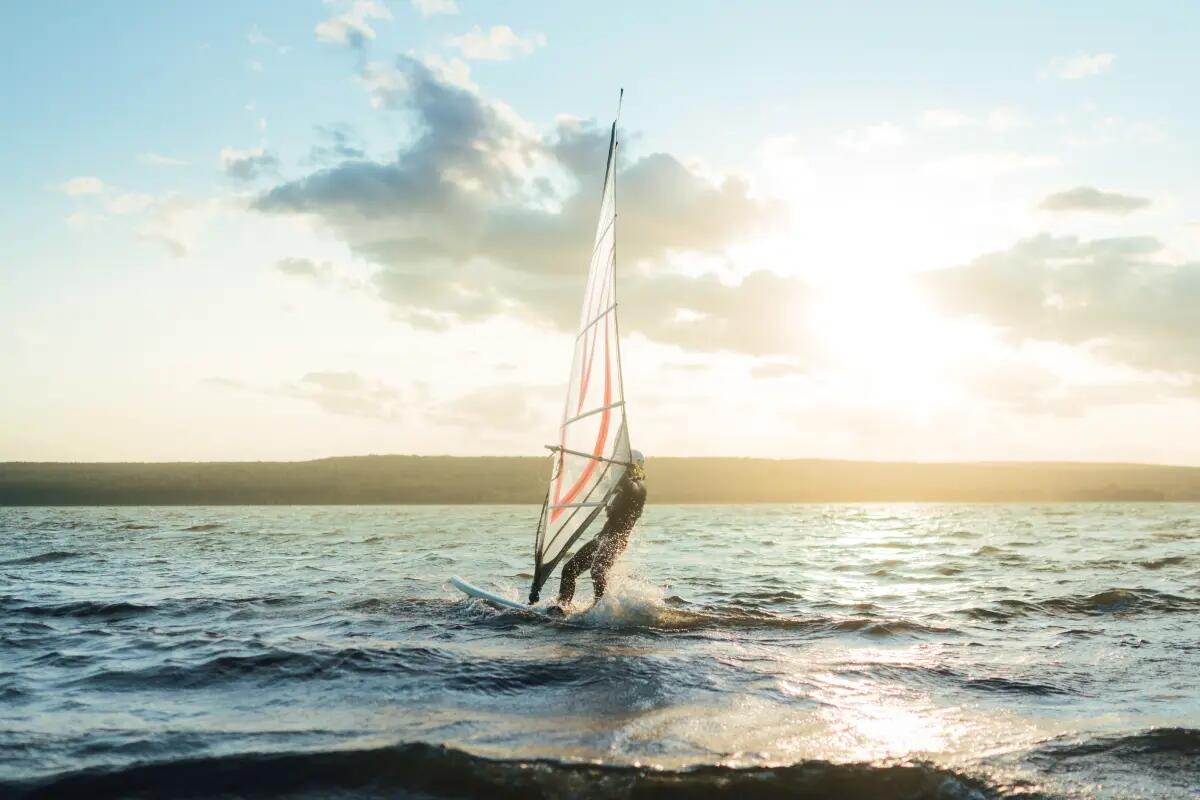 osoba płynąca na desce windsurfingowej trzymając żagiel windsurfingowy