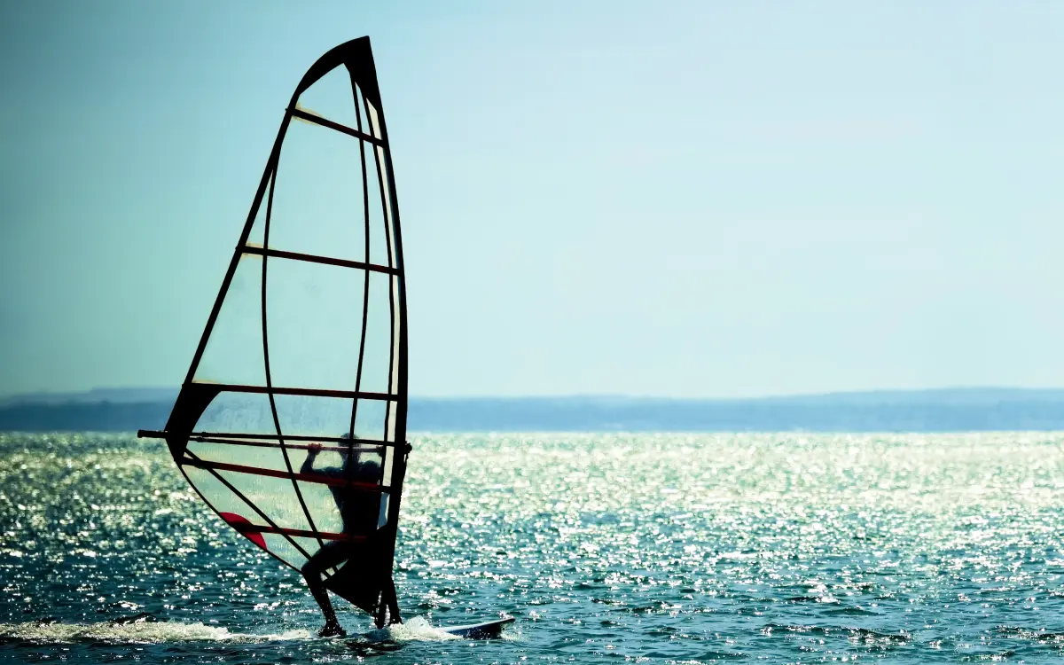 mężczyzna pływający na desce windsurfingowej  trzymając żagiel windsurfingowy