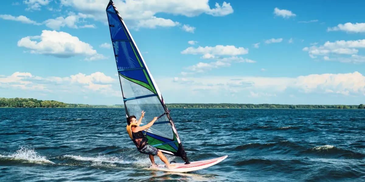 mężczyzna w kamizelce asekuracyjnej pływający na desce windsurfingowej