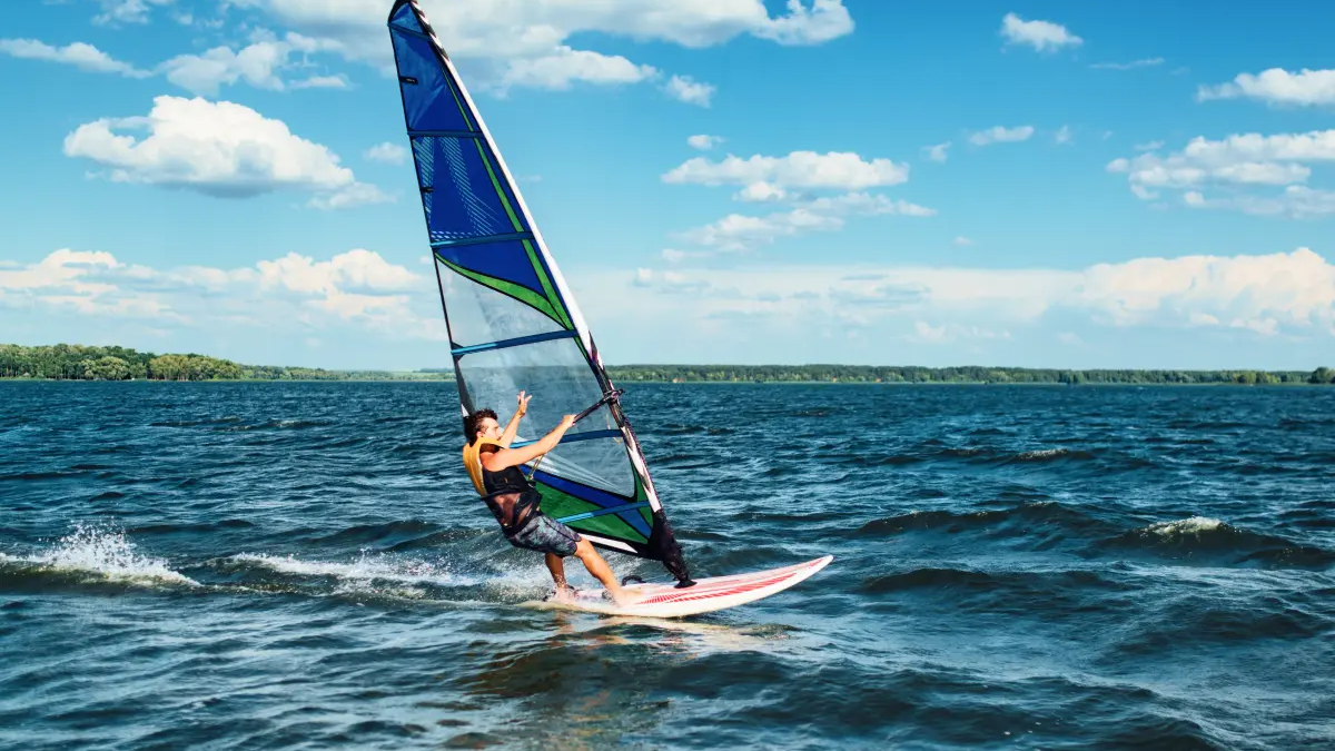 mężczyzna płynący na desce windsurfingowej trzymając się żagla