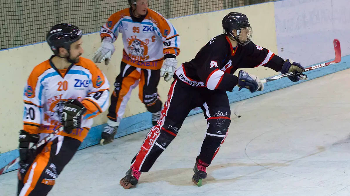 mężczyźni w kaskach i odzieży hokejowej grający w hokeja in-line na hali