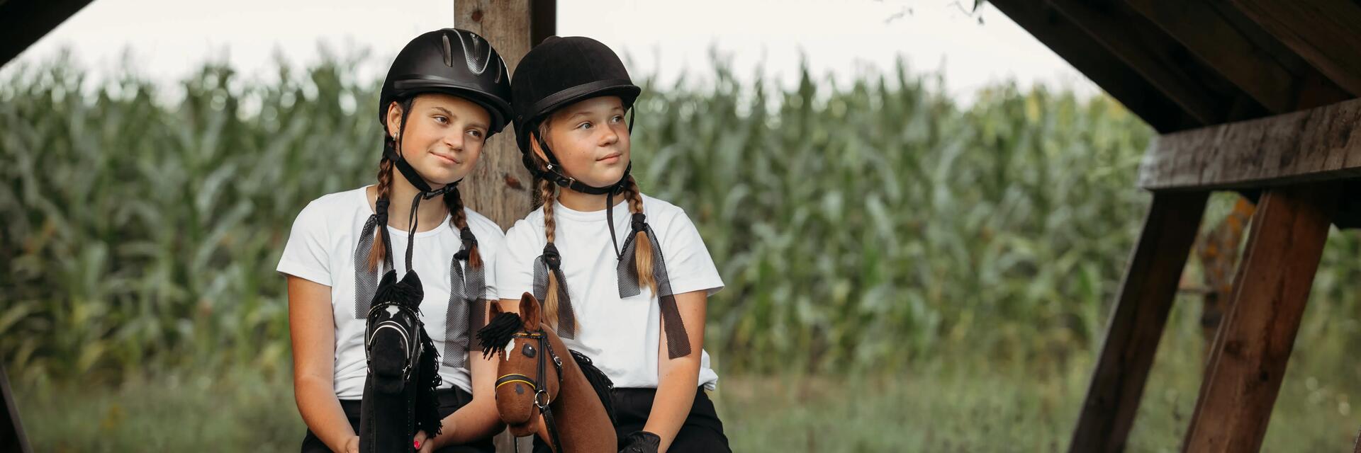 zwei junge Mädchen in einer Hütte. Mit Helm auf dem Kopf mit Hobbyhorse in der hand 