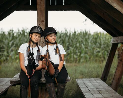 zwei junge Mädchen in einer Hütte. Mit Helm auf dem Kopf mit Hobbyhorse in der hand