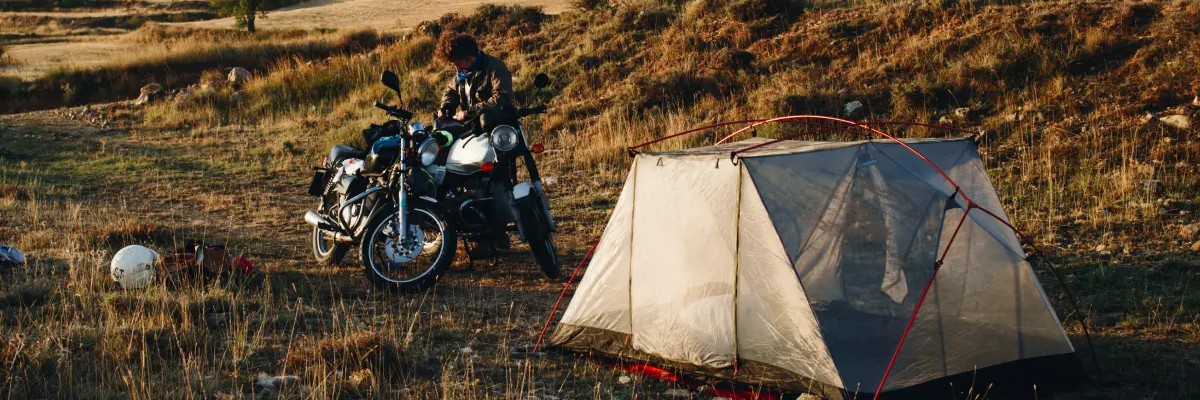 Motocyklista stojący w plenerze przy motorze w pobliżu rozłożonego namiotu na motocykl