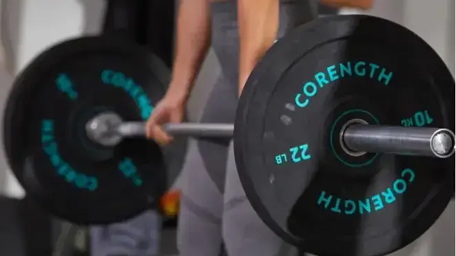 Kobieta w stroju sportowym trzymająca sztangę z cieżarami