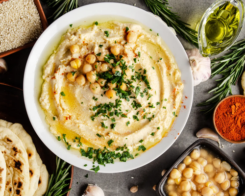 Hummus wegański zamiennik masła umieszczony w białej misce leżacy w otoczeniu wegańskich produktów spożywczych