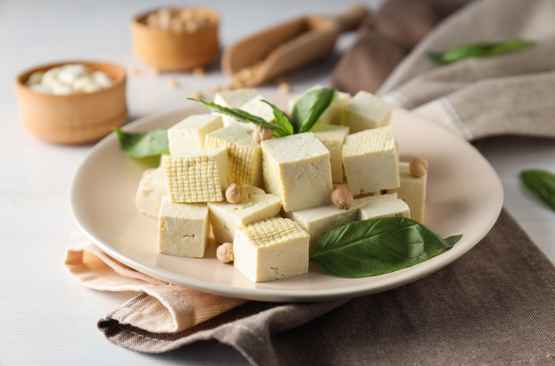 Wegańskie tofu pokrojone w kostkę umieszczone na białym talerzu leżącym na ściereczce
