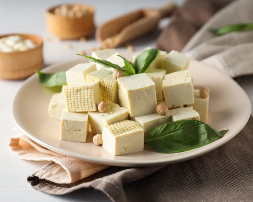 Talerz z produktem wegańskim pokrojonym w kosteczkę tofu ozdobionym liśćmi bazylii i orzechami laskowymi