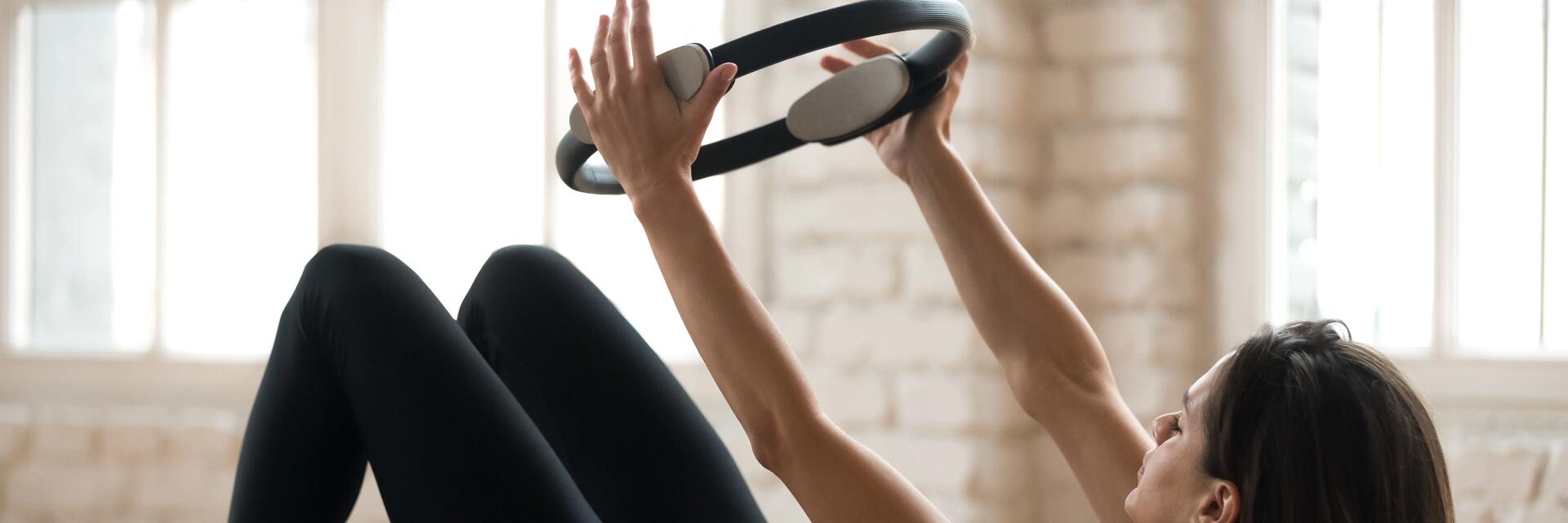 Kobieta leżąca na macie ćwicząca z obręczą do pilatesu